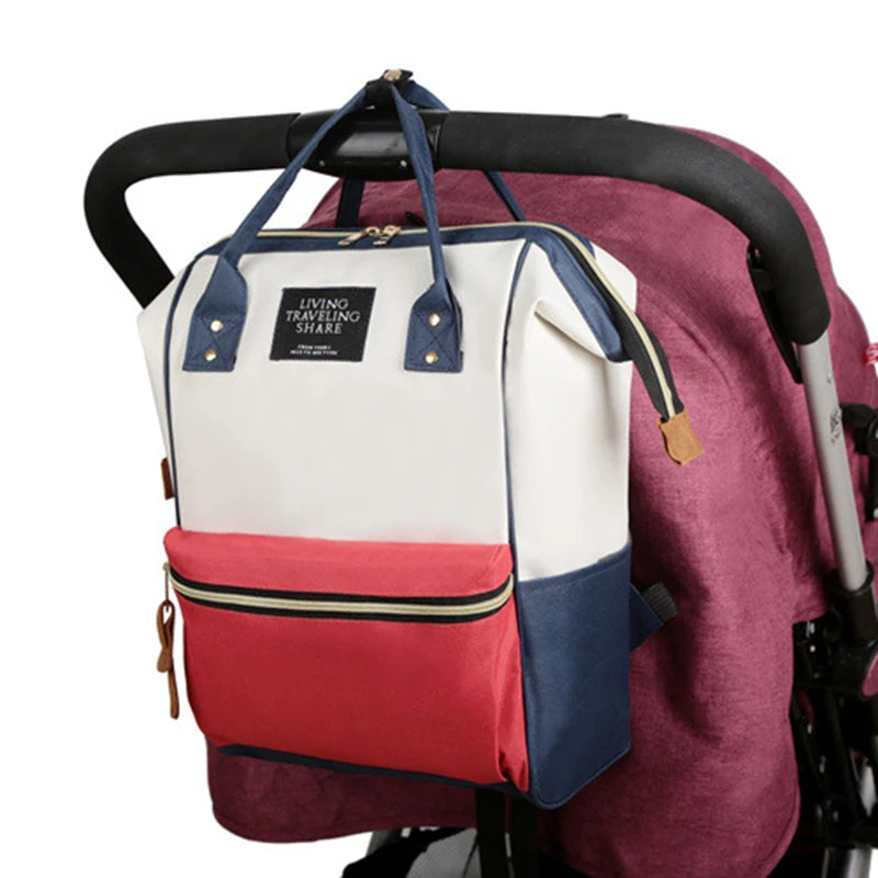 Multifunctional canvas diaper bag in white, red, and navy, hanging on a stroller.