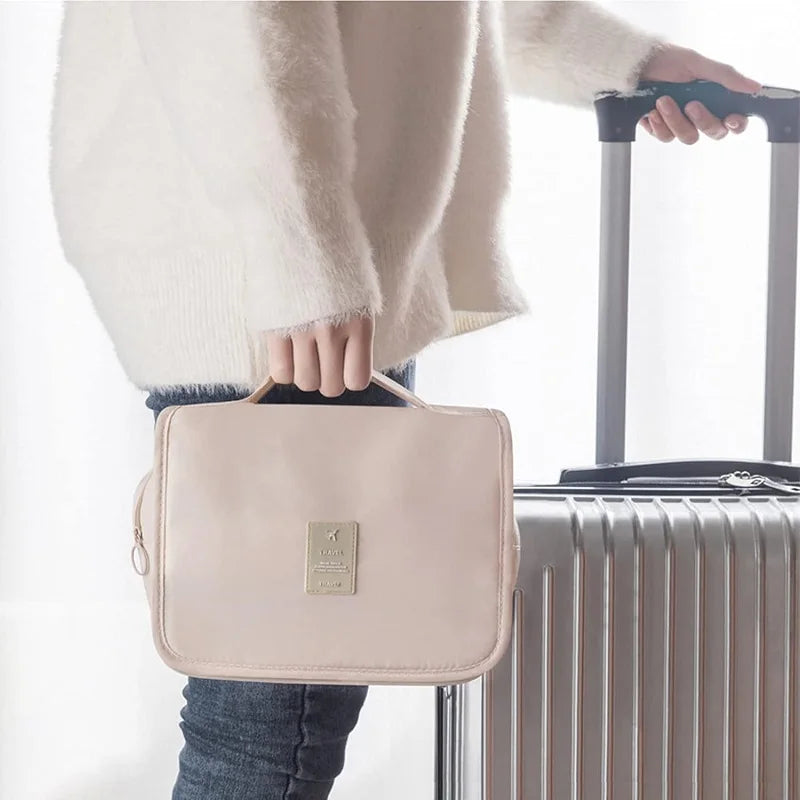 Beige waterproof polyester travel toiletry bag with handle, held by a person next to a suitcase.
