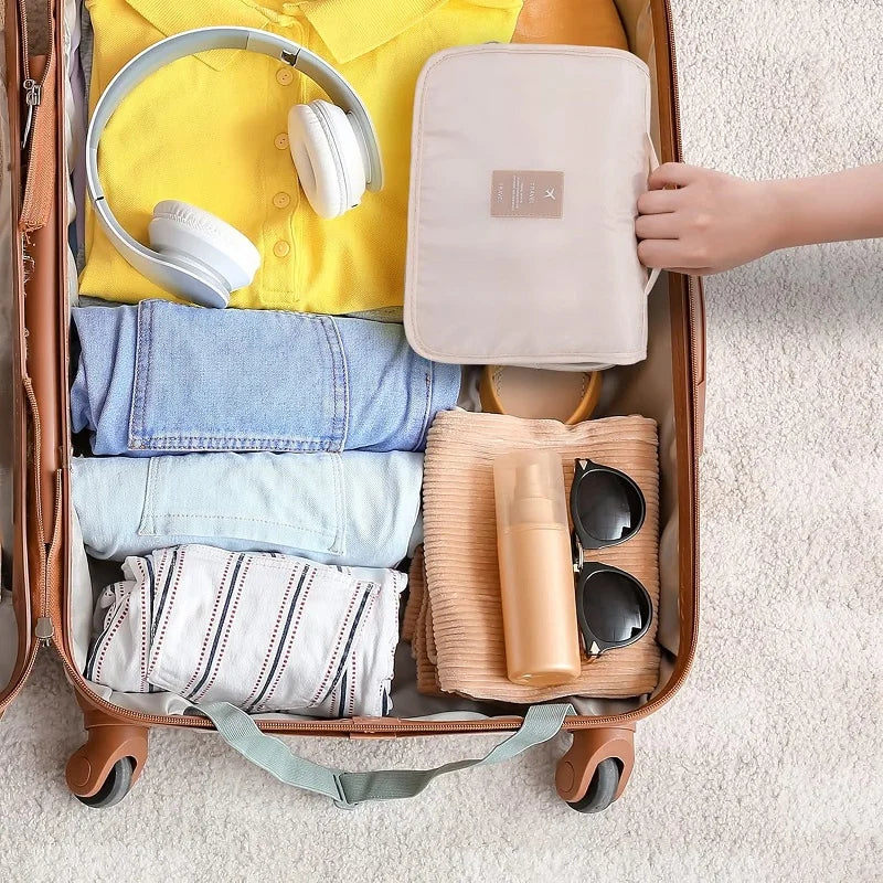 Beige waterproof travel toiletry bag with hanging hook, folded inside a suitcase with clothes and accessories.