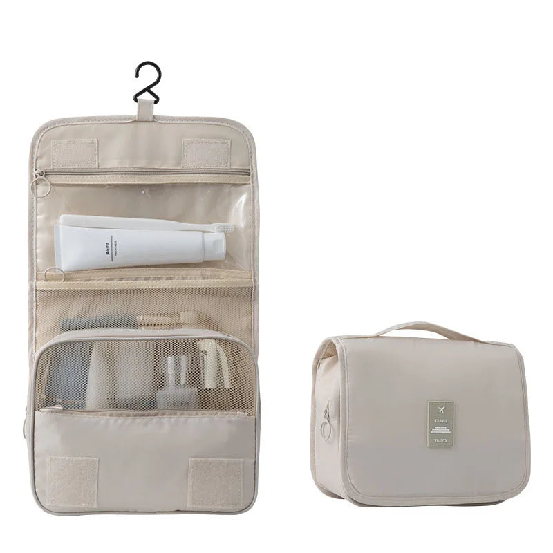Beige waterproof travel toiletry bag, open with clear and mesh pockets, and closed with a handle and travel tag.