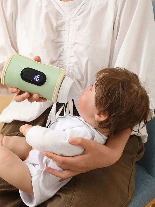Parent holding a baby, feeding from a light green portable USB bottle warmer with a digital display.